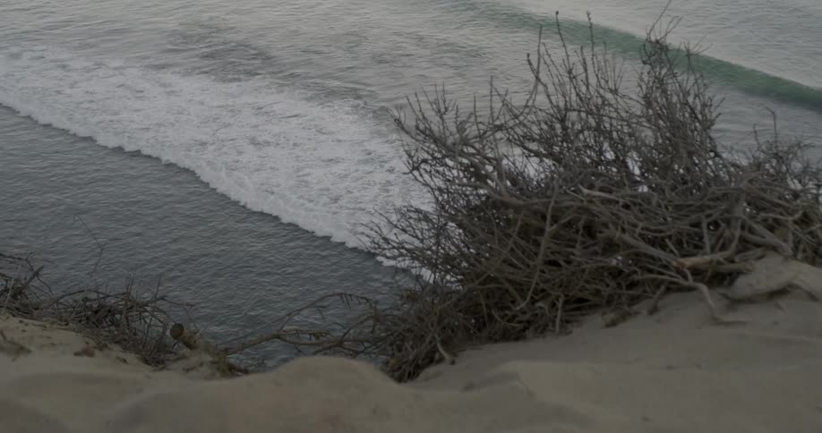 A view of waves crashing ashore from the top of a sandy cliff
