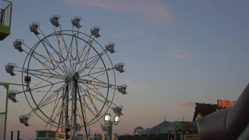A ferris wheel turns slowly as the sun sets at an amusement park