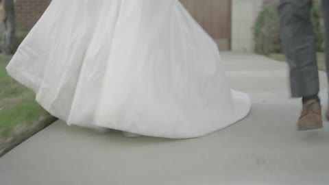 A bride and groom run down the sidewalk in front of a church