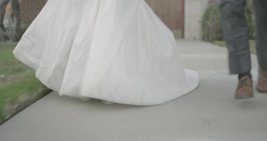 A bride and groom run down the sidewalk in front of a church