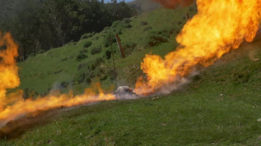 A gas container sitting in a smoldering campfire explodes on a grassy hillside