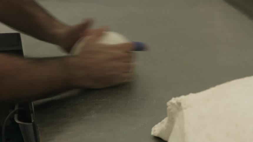 A man rolls dough into a ball on a countertop