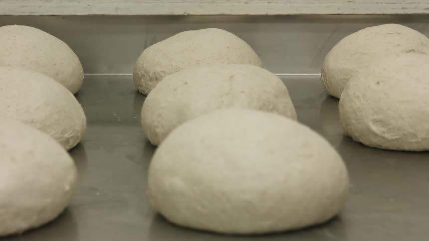 Balls of dough resting on a stainless steel counter
