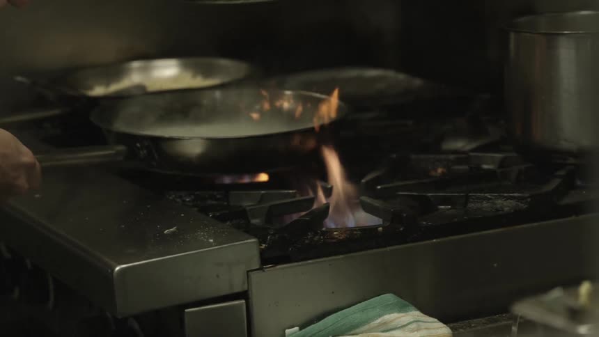 A chef cooking with multiple frying pans