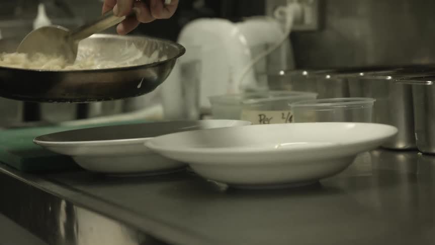 A man cooking scrambled eggs and putting them in shallow bowls