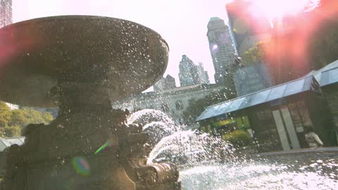Water spraying from a fountain and splashing into a pool in an urban area on a sunny day