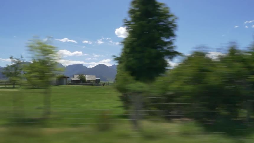 Moving down a road next to a field with mountains in the background
