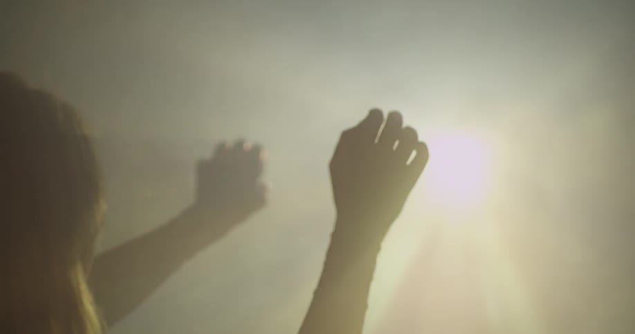A woman is raising her hands towards a light