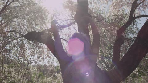 A woman slowly spins around under the shade of a tree