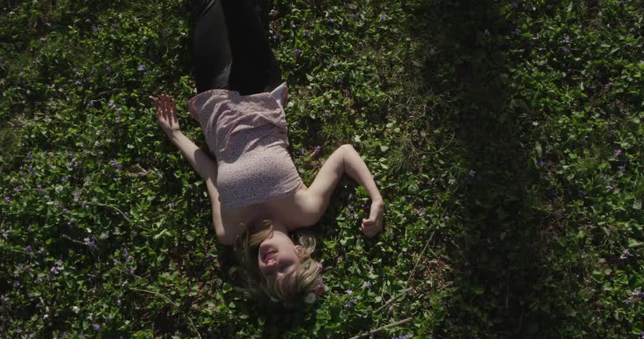 Smiling woman rolling over and laying in the green grass