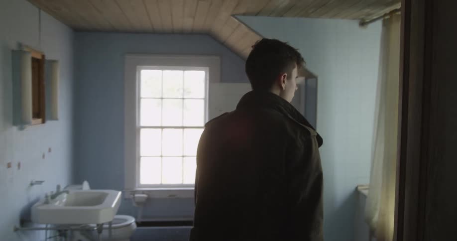 A man enters a household bathroom and looks into the bathtub