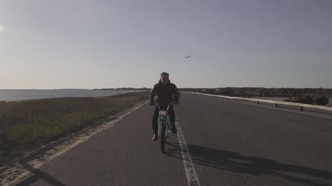 A man riding a moped down a road that runs alongside the ocean