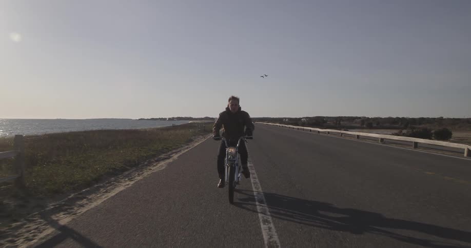 A man riding a moped down a road that runs alongside the ocean