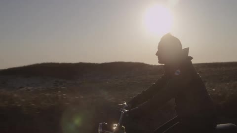 A motorcyclist rides through a sunny, rural area