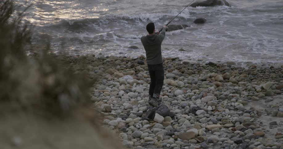 A man fishes on a rocky beach