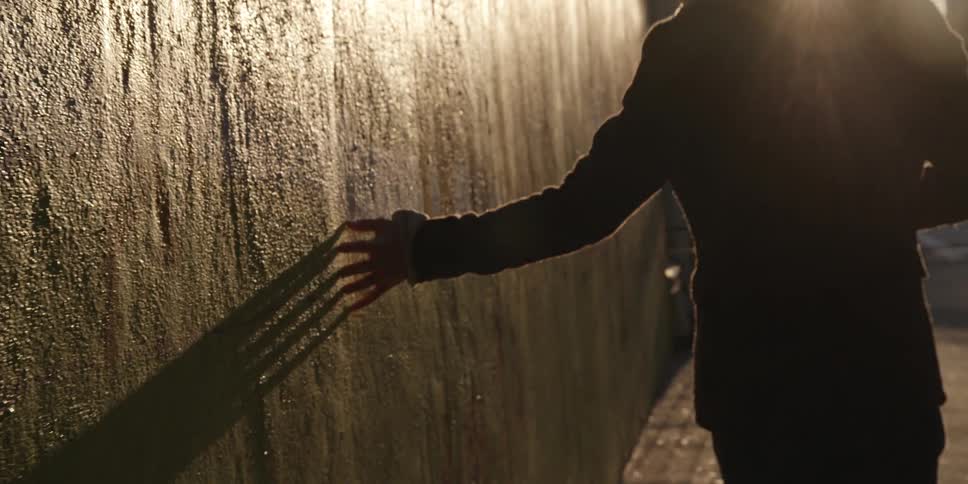 A woman dragging her fingers along a wall as she walks down the street