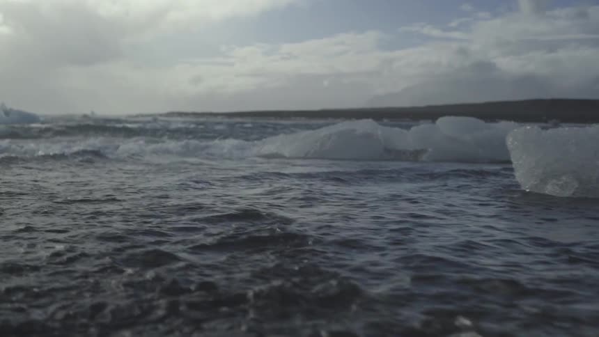 Beach waves splash onto chunks of ice