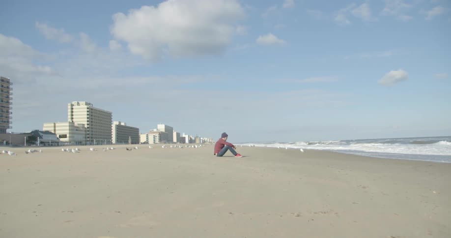 A man sits on the beach with buildings in the background