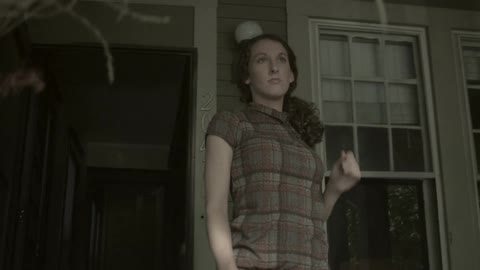 A young woman walks out from a house onto a front porch