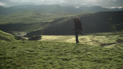A woman with a camera walks through a sunny valley