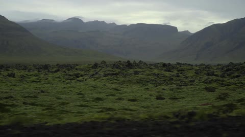 View of a rocky pasture with mountains in the background under a cloudy sky