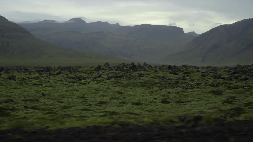 View of a rocky pasture with mountains in the background under a cloudy sky