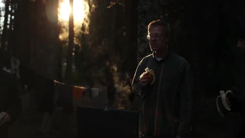 Two men stand around a campfire in a campsite
