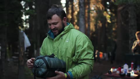 A man laughing and adjusting straps on a bag at a campsite