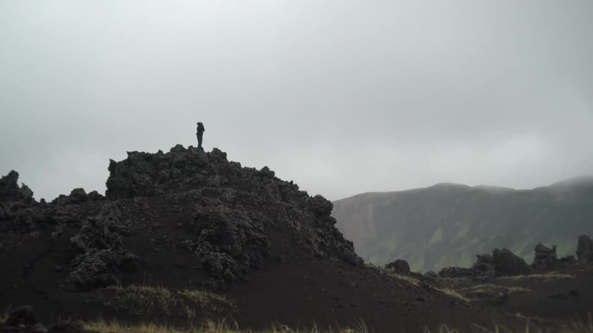 Someone standing on top of a rocky cliff with mountains in the background