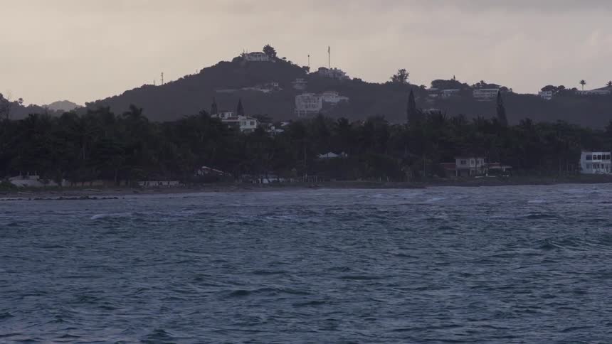 Choppy water flows in front of a hill with buildings