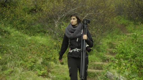 A woman with a tripod walks through the wilderness