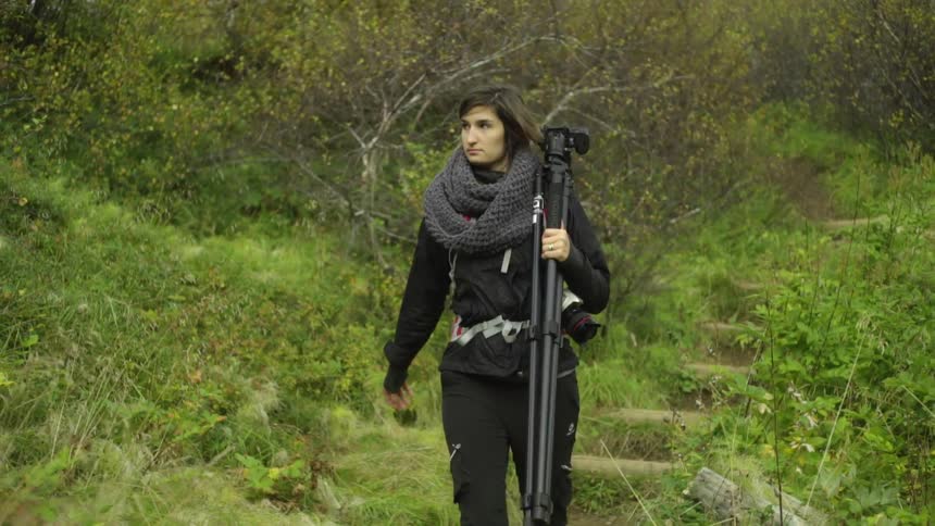 A woman with a tripod walks through the wilderness