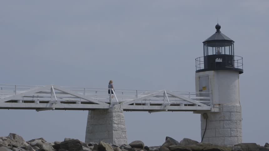 A woman runs across a bridge towards a lighthouse