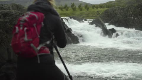 A hiker photographs a swirling waterfall and river