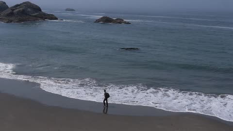A man wearing a backpack walking along the beach as waves roll in