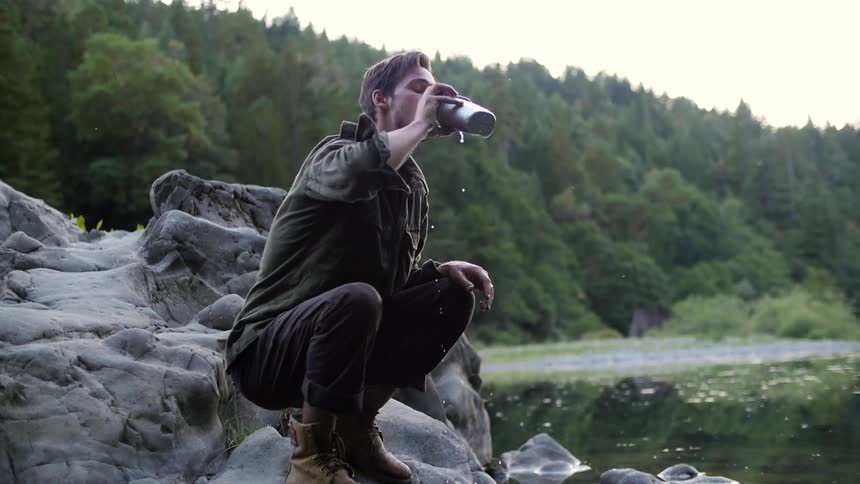 A man dips a canteen into a river and takes a drink