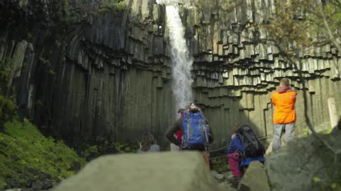 A waterfall cascades over a cliff as hikers watch