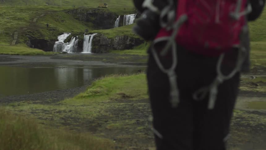 A hiker approaches a waterfall and lake