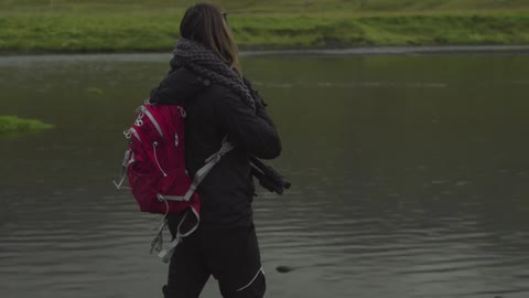 A woman with a camera walks by a lake