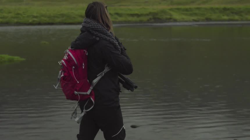 A woman with a camera walks by a lake