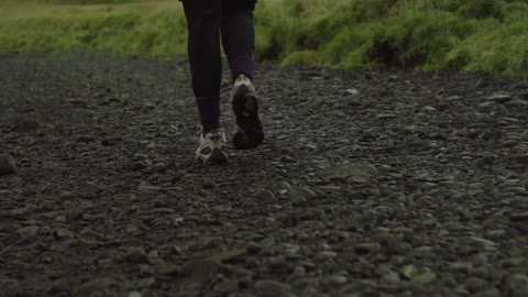 A person walks on gravel near grass