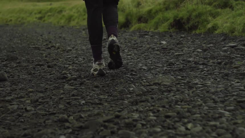 A person walks on gravel near grass