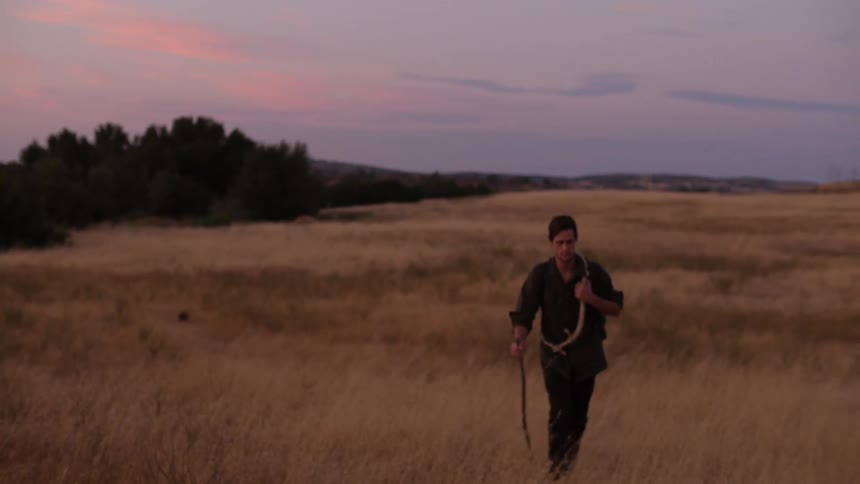 A man walks alone in a grass field at dawn
