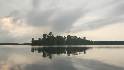 A tiny tree covered island is reflected in the waters surface