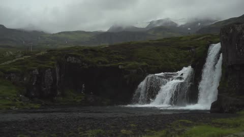 A waterfall flows near a grassy mountainside