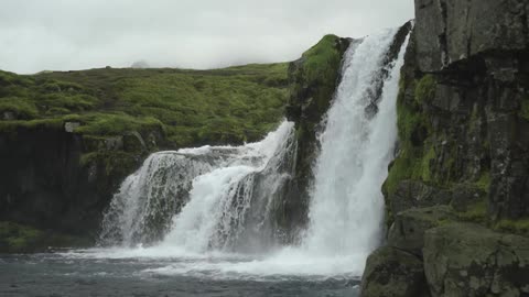 Waterfalls cascading down a grassy mountain cliff with clouds in the sky