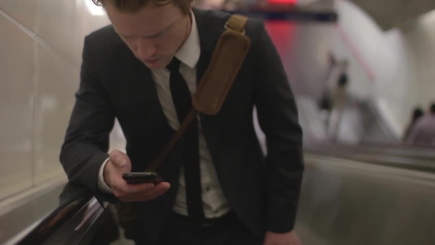 A man checks his phone while riding up an escalator