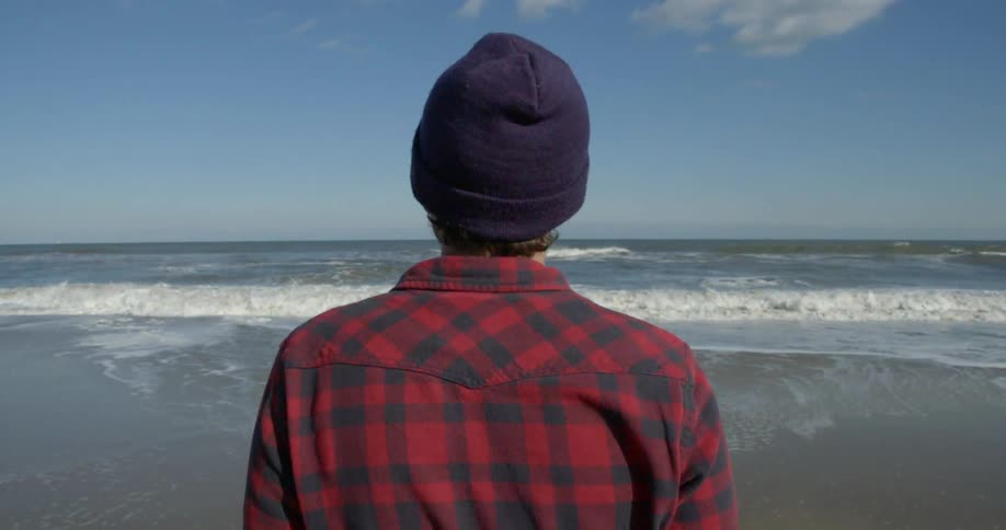 A man stands on the sands of a beach watching the waves roll in