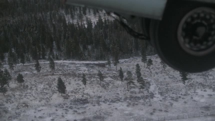 The landing gear going inside a plane at take off in a snowy, wooded area