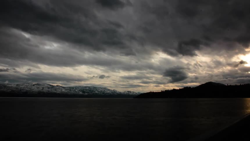 Dark clouds move over a mountain range and body of water